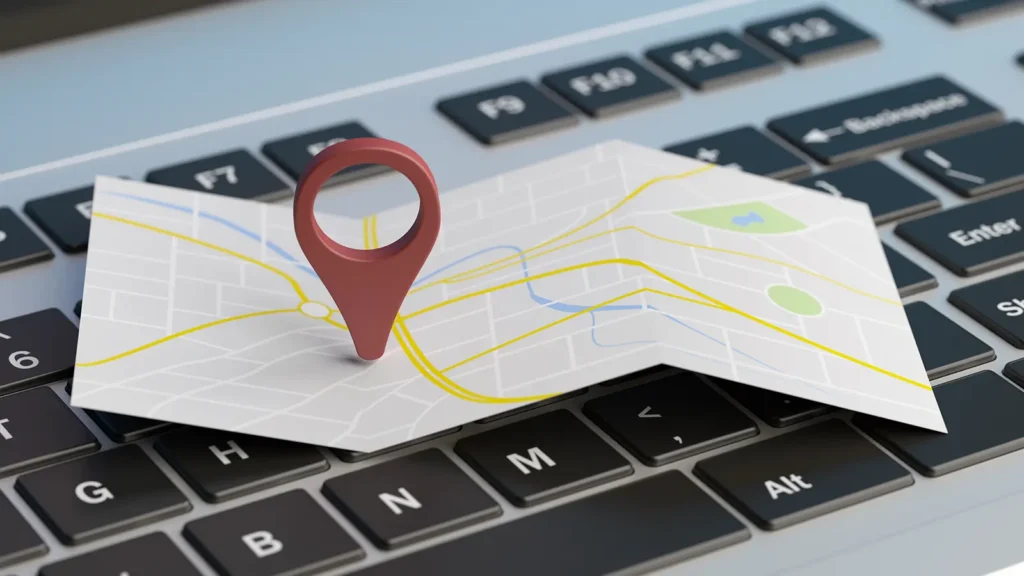 Papierowa mapa z kolorowymi liniami i dużą czerwoną pinezką lokalizacji znajduje się na klawiaturze komputera, symbolizując cyfrową nawigację lub mapy online - idealne dla 2025 poradnika na temat konfigurowania Profilu Firmy w Google.